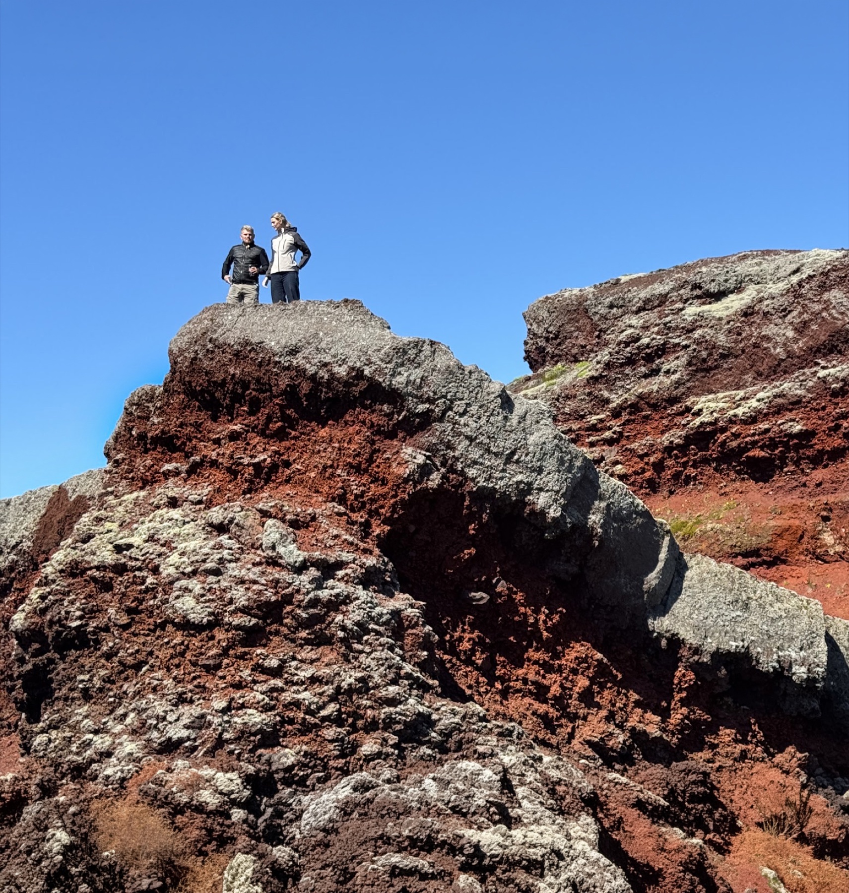 Two people exploring red volcanic rock in Iceland